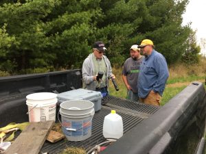 Agriculture Agent Ken Schroeder demonstrating testing equipment for two other individuals at the back of an open truck bed. 